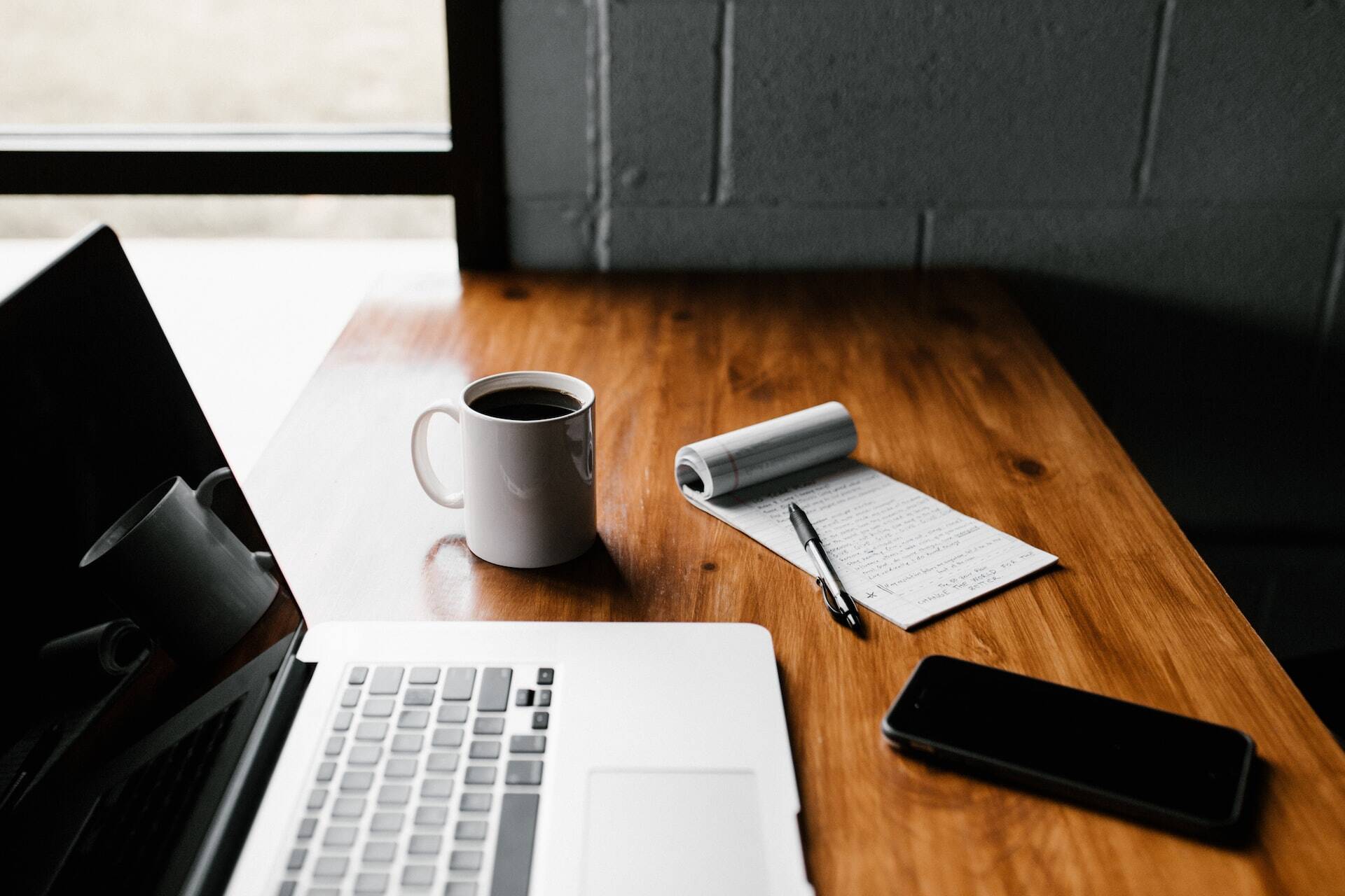 Macbook next to a coffee mug, some notes and a smartphone