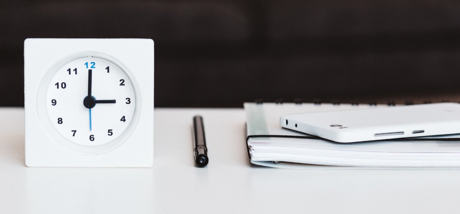 A clock next to a pen and a journal