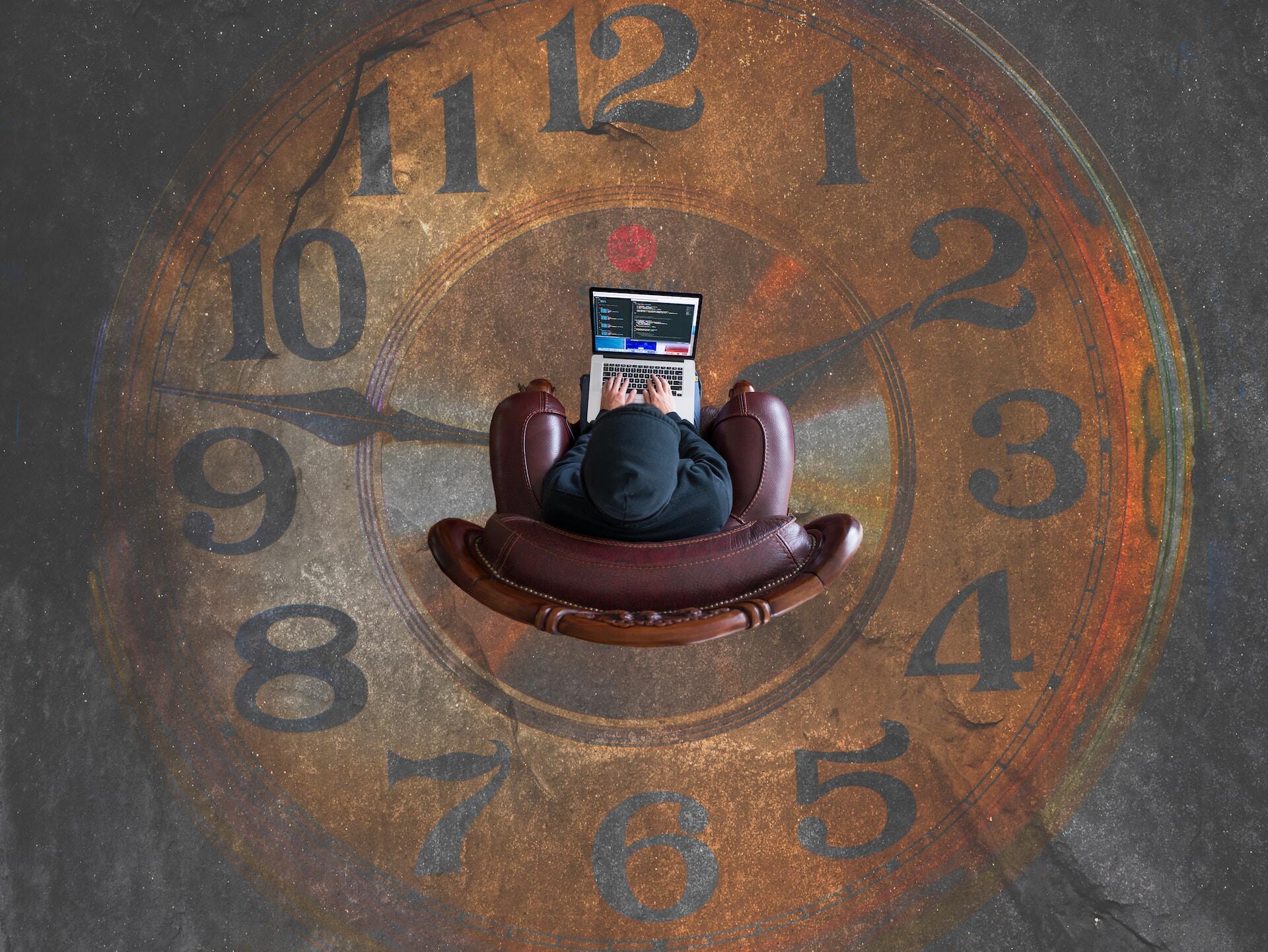 Man working in a macbook sitting in a chair inside a clock paint on the floor